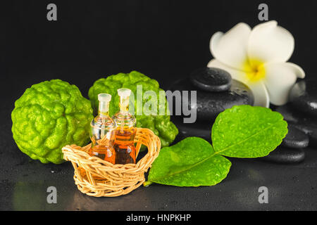Spa-Konzept von Bergamotte, Blatt-, Duftöl, weiße Plumeria und Zen Basaltsteinen mit Wasser Tau auf schwarzem Hintergrund, Nahaufnahme Stockfoto