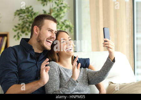 Lässige Brautpaar in einem Handy video Gruß fordere Linie sitzen auf einem Sofa im Wohnzimmer zu Hause mit einem Fenster im Hintergrund Stockfoto