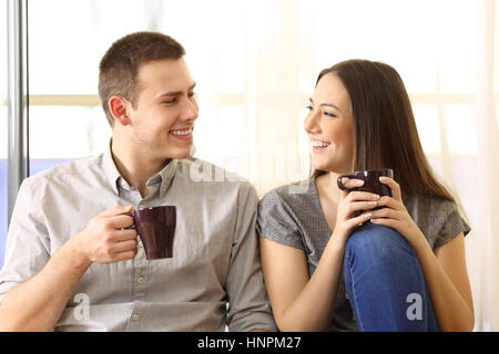 Vorderansicht eines glücklichen Paares sprechen und trinken Kaffee sitzen auf dem Boden in der Nähe eines Fensters zu Hause Stockfoto