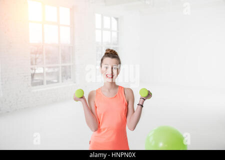 Portrait von junge Frau in Sportkleidung mit Hanteln und Fitness-Ball im weißen Fitnessstudio Stockfoto