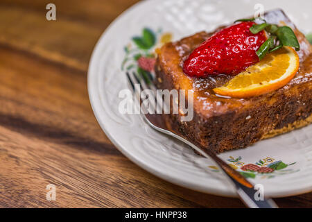 Stück Obst-Torte mit Erdbeeren und Zitrone auf Untertasse mit Gabel auf Holztisch Stockfoto