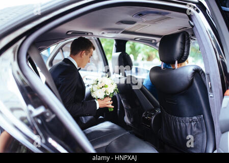 Glückliche schöne Braut, sitzen im Hochzeitsauto mit einem Blumenstrauß Stockfoto
