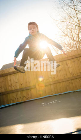 9-jähriger Junge springen auf einem Trampolin in seinem Garten. Stockfoto