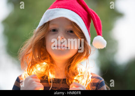 Ein kleines Mädchen gekleidet in einem Santa Hut und Fee Weihnachtsbeleuchtung Stockfoto