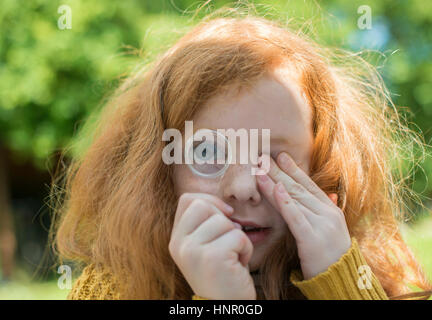 Ein kleines Mädchen auf der Suche durch ein Vergrößerungsglas in ihrem Garten Stockfoto