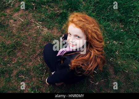 Ein kleines Mädchen mit roten Heair saß auf dem Rasen Stockfoto