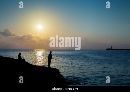 Valletta, Malta - in den frühen Morgenstunden zwei Fischer warten auf einen Happen in Sliema Tigne Point mit Wellenbrecher Leuchtturm im Hintergrund Stockfoto