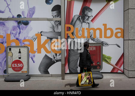 Eine Dame Shopper Tragetasche von Safeway-Supermarkt geht vorbei an einem Sainsbury Plakat am 13. Februar 2017, in der City of London, Großbritannien. Stockfoto