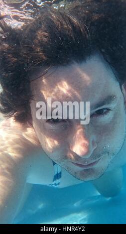 Mann im Schwimmbad unter Wasser machen Selfie. Männchen von Closeup Portrait Vorderansicht unter Wasser tauchen. Stockfoto