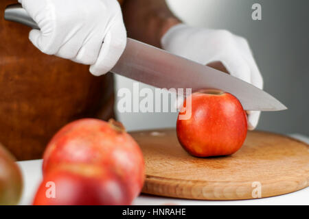 Close-up auf Händen in weißen Handschuhen einen Apfel mit Hilfe von großen scharfen Messer schneiden Stockfoto