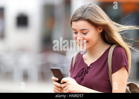 Glückliches Mädchen gehen und Schreiben von Nachrichten auf dem Handy auf der Straße Stockfoto