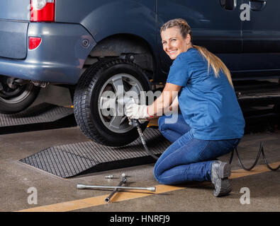 Happy Mechanikerin Festsetzung Reifen mit pneumatischen Schraubenschlüssel Stockfoto