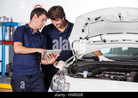 Mechanik diskutieren während der Verwendung von Tablet PC mit dem Auto Stockfoto