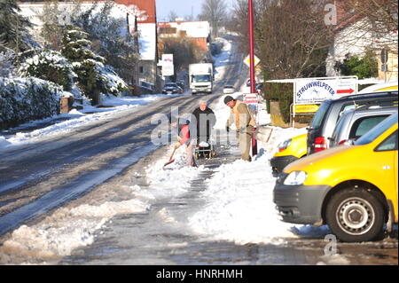 Worms, Deutschland - 9. Dezember 2010: alte Frau zu Fuß auf verschneiten Straße während der öffentlichen Beschäftigten Gehweg Reinigung Stockfoto