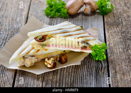 Gedrückt und gerösteten doppelte Panini mit Schinken, Käse und Pilzen auf Butterbrotpapier auf einem Holztisch serviert Stockfoto