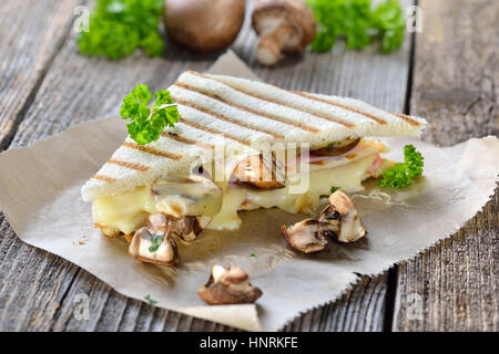 Gedrückt und gerösteten doppelte Panini mit Schinken, Käse und Pilzen auf Butterbrotpapier auf einem Holztisch serviert Stockfoto