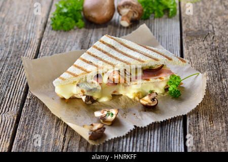 Gedrückt und gerösteten doppelte Panini mit Schinken, Käse und Pilzen auf Butterbrotpapier auf einem Holztisch serviert Stockfoto