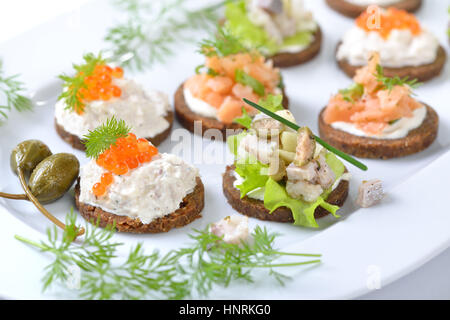 Lecker Fisch Fingerfood mit geräuchertem Lachs Tartar, Forellen-Mousse mit Kaviar und Heringssalat auf Runde Pumpernickel Brot Stockfoto