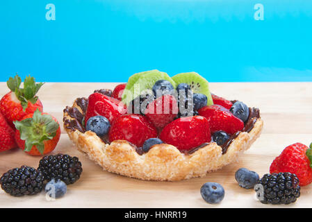 Frisches Obst Törtchen mit Blume geformt Tortekruste bestreut mit Zuckerkristallen überzogen mit Schokolade gefüllt mit Vanillesoße, garniert mit frischen Erdbeeren, Stockfoto