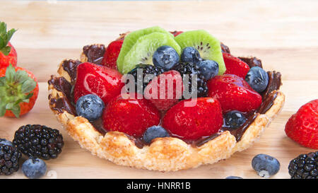 Frisches Obst Törtchen mit Blume geformt Tortekruste bestreut mit Zuckerkristallen überzogen mit Schokolade gefüllt mit Vanillesoße, garniert mit frischen Erdbeeren, Stockfoto