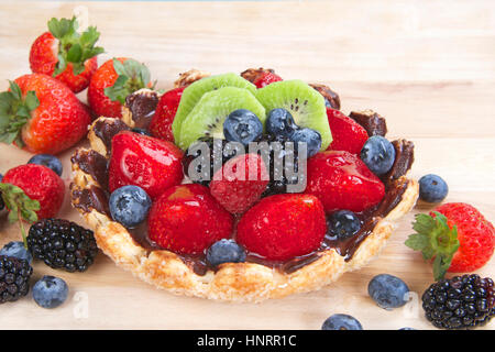 Frisches Obst Törtchen mit Blume geformt Tortekruste bestreut mit Zuckerkristallen überzogen mit Schokolade gefüllt mit Vanillesoße, garniert mit frischen Erdbeeren, Stockfoto