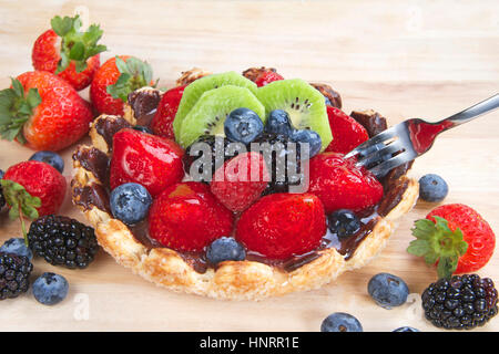 Frisches Obst Törtchen mit Blume geformt Tortekruste bestreut mit Zuckerkristallen überzogen mit Schokolade gefüllt mit Vanillesoße, garniert mit frischen Erdbeeren, Stockfoto