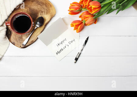 Overhead Schuss eine glückliche Mutter Tageskarte mit Blumenstrauß Tulpe mit schwarzen Kaffee und einer gemütlichen Strick Decke über weiße Holz Tischplatte werfen. Wohnung Stockfoto