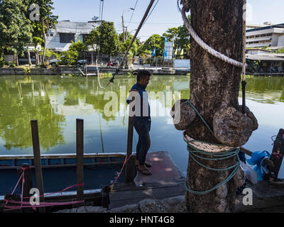 Thepharak, Samut Prakan, Thailand. 16. Februar 2017. Ein Fährmann, der seinem kleinen Boot als eine Fähre benutzt wartet auf Fluggäste am Khlong Samrung am Stadtrand von Bangkok. Der Bootsmann zieht es über ein System von Seilen und Rollen. Er arbeitet auf dem Boot, seit er ein Kind war. Kleine Fähren wie dies früher häufig in Bangkok aber viele Khlongs (die Kanäle, die verwendet, um Bangkok zu durchkreuzen) ausgefüllt und Brücken über die verbleibenden Khlongs wurden. Jetzt gibt es nur eine Handvoll Fähren links. Diese Fähre lädt 2 Baht (das Äquivalent von ca.. 06¢ US) pro Person Stockfoto