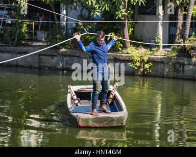 Thepharak, Samut Prakan, Thailand. 16. Februar 2017. Ein Fährmann zieht sein kleine Boot, die er als eine Fähre in Khlong Samrong, am Stadtrand von Bangkok benutzt. Der Bootsmann zieht es über ein System von Seilen und Rollen. Er arbeitet auf dem Boot, seit er ein Kind war. Kleine Fähren wie dies früher häufig in Bangkok aber viele Khlongs (die Kanäle, die verwendet, um Bangkok zu durchkreuzen) ausgefüllt und Brücken über die verbleibenden Khlongs wurden. Jetzt gibt es nur eine Handvoll Fähren links. Diese Fähre lädt 2 Baht (das Äquivalent von ca.. 06¢ US) pro Person zu Tak Stockfoto