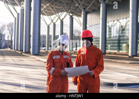 glückliches Team von jungen Ingenieuren ein Bauprojekt zu diskutieren und lächelnd. Der Verschleiß Overalls und Helme. Moderne Business-Hintergrund Stockfoto