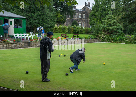 Teilnehmer und Zuschauer (im Regen) auf ein Krone grün-Bowling-Spiel auf dem Dorfplatz Bowling - Burley In Wharfedale, West Yorkshire, England. Stockfoto