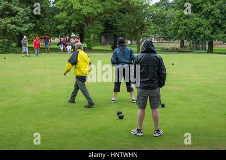 Teilnehmer und Zuschauer (im Regen) auf ein Krone grün-Bowling-Spiel auf dem Dorfplatz Bowling - Burley In Wharfedale, West Yorkshire, England. Stockfoto