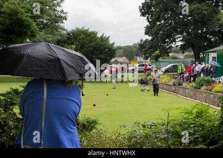 Teilnehmer und Zuschauer (im Regen) auf ein Krone grün-Bowling-Spiel auf dem Dorfplatz Bowling - Burley In Wharfedale, West Yorkshire, England. Stockfoto