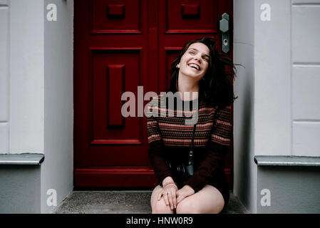 Lachende Frau kaukasischen sitzen in Tür Stockfoto