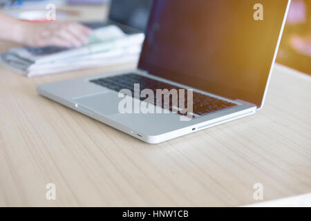 Laptop-Computer auf Holztisch mit Hand auf Zeitung Stockfoto