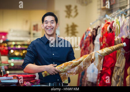 Lächelnde chinesische Mann posiert mit Stoff im store Stockfoto