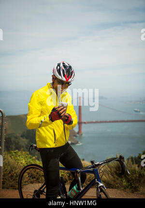 Hispanic Mann auf dem Fahrrad SMS auf Handy an waterfront Stockfoto