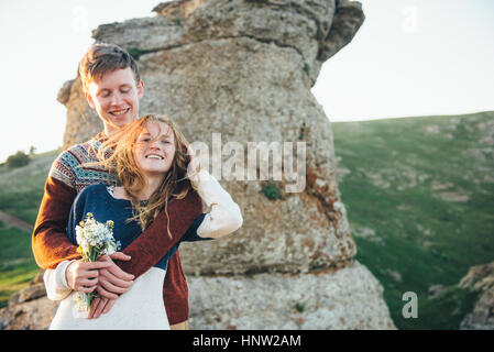 Kaukasische paar umarmt in der Nähe von Felsen mit Blumenstrauß Stockfoto