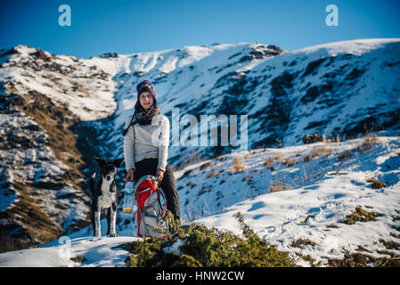 Kaukasische Frau posiert mit Hund und Rucksack auf Berg Stockfoto