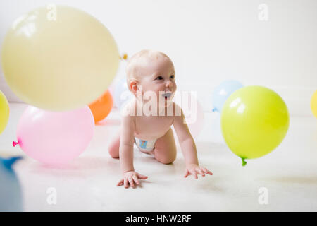 Kaukasische Babyjungen kriecht am Boden beobachten Ballons Stockfoto