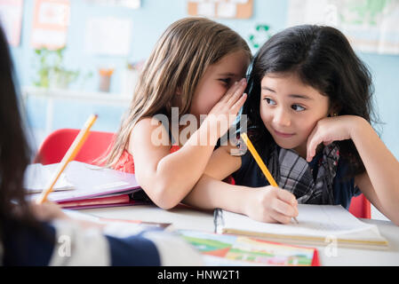 Mädchen Flüstern an Mitschüler in der Schule Stockfoto