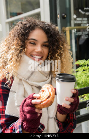 Lächelnd Mischlinge Frau zeigt Donut und Kaffeetasse Stockfoto