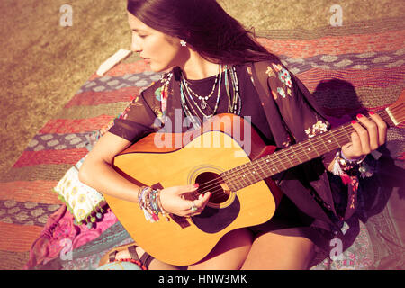 Asiatische Frau sitzen auf Decke, Gitarre spielen Stockfoto