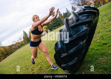 Kaukasische Frau schwere Reifen bergauf schieben Stockfoto