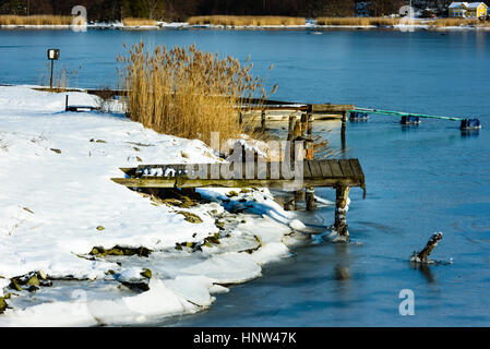 Kleine hölzerne Pier in gefrorenen Meereis und Schnee. Coastal Winterlandschaft. Lage Hjortahammar in Blekinge, Schweden. Stockfoto