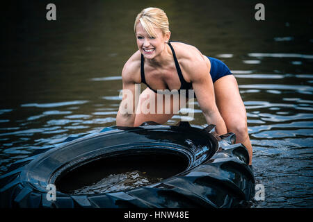 Kaukasische Frau heben schwere Reifen in See Stockfoto