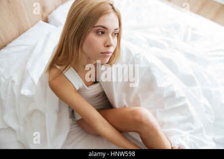 Draufsicht der nachdenklichen hübsche junge Frau sitzen und denken auf Bett zu Hause Stockfoto