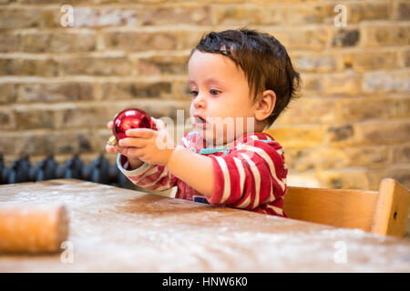 Baby Boy mit Weihnachtskugel am Tisch spielen Stockfoto