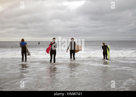 Rückansicht des vier junge Erwachsene Surfer tragen Surfbretter ins Meer auf Rockaway Beach, New York, USA Stockfoto