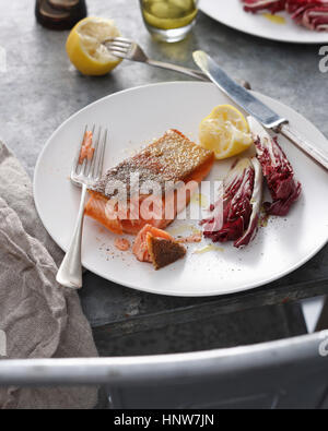 Knusprige Haut Forelle mit Zitrone und Radicchio auf Teller, Nahaufnahme Stockfoto